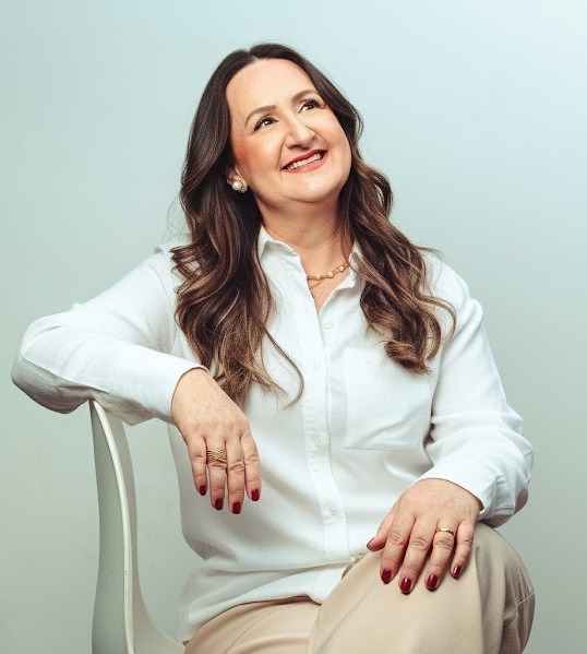 Suzi Vassoler sorrindo, sentada em uma cadeira branca